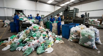 Processo inicial de como é feita a reciclagem de sacolas com trabalhadores separando plástico em uma esteira transportadora.