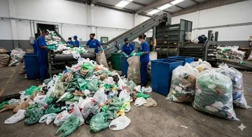 Processo inicial de como é feita a reciclagem de sacolas com trabalhadores separando plástico em uma esteira transportadora.